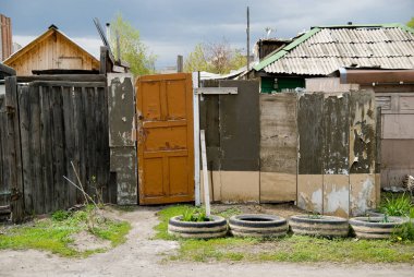 Arka planda avlunun ahşap kapısı, kötü tahtalardan oluşan bir çit. Köy kenar mahalleleri