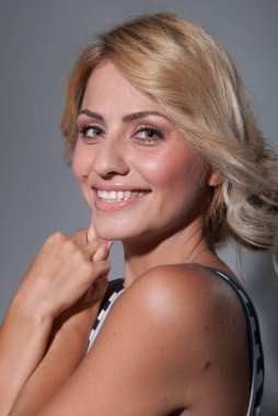 Koyu gri arka planda kameraya bakan gülümseyen genç bir kadının portresi.