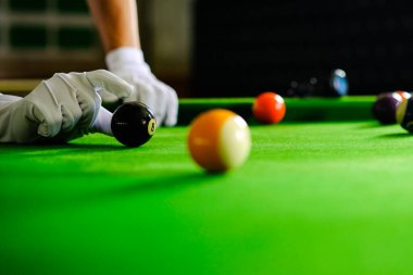 Adamın eli ve Cue kolu bilardo oynuyor ya da yeşil bir bilardo masasında bilardo topu fırlatmaya hazırlanıyor. Yeşil frizde renkli bilardo topları