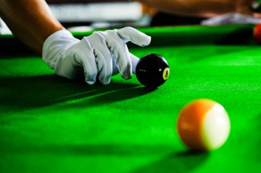 Adamın eli ve Cue kolu bilardo oynuyor ya da yeşil bir bilardo masasında bilardo topu fırlatmaya hazırlanıyor. Yeşil frizde renkli bilardo topları