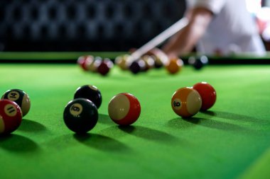 Adamın eli ve Cue kolu bilardo oynuyor ya da yeşil bir bilardo masasında bilardo topu fırlatmaya hazırlanıyor. Yeşil frizde renkli bilardo topları