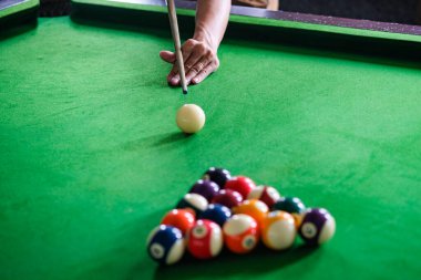 Adamın eli ve Cue kolu bilardo oynuyor ya da yeşil bir bilardo masasında bilardo topu fırlatmaya hazırlanıyor. Yeşil frizde renkli bilardo topları