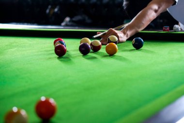 Adamın eli ve Cue kolu bilardo oynuyor ya da yeşil bir bilardo masasında bilardo topu fırlatmaya hazırlanıyor. Yeşil frizde renkli bilardo topları