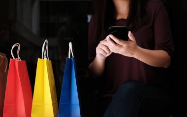 Asyalı kızlar ellerinde alışveriş torbaları tutuyor. Alışveriş merkezinin ellerinde cep telefonunun boş fotokopi ekranını tutan tüketim yaşam tarzı kavramı 
