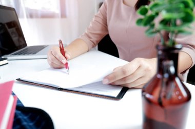 Sınıfta ders sırasında dizüstü bilgisayar ve not defteriyle masada oturan genç bir kadın ders çalışıyor.