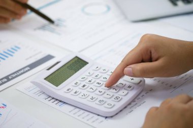 Yatırım çizelgelerini analiz eden ve belgelerin üzerindeki hesap makinesi tuşlarına basan bir işadamı. Muhasebe Kavramı
