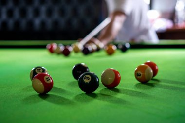Adamın eli ve Cue kolu bilardo oynuyor ya da yeşil bir bilardo masasında bilardo topu fırlatmaya hazırlanıyor. Yeşil frizde renkli bilardo topları