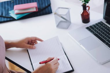 Sınıfta ders sırasında dizüstü bilgisayar ve not defteriyle masada oturan genç bir kadın ders çalışıyor.