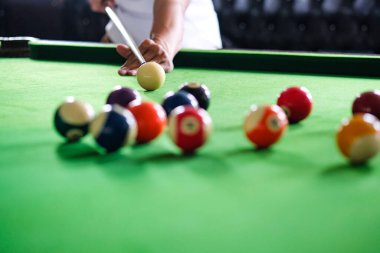 Adamın eli ve Cue kolu bilardo oynuyor ya da yeşil bir bilardo masasında bilardo topu fırlatmaya hazırlanıyor. Yeşil frizde renkli bilardo topları