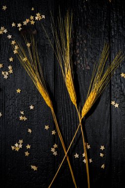 Yatay bileşim, buğday kulaklı, arka planda siyah yanık tahtalar dağınık hamur yıldızları ve bej kumaşlı. Aile mutluluğu kavramı