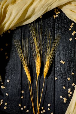 Yatay bileşim, buğday kulaklı, arka planda siyah yanık tahtalar dağınık hamur yıldızları ve bej kumaşlı. Aile mutluluğu kavramı