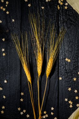 Yatay bileşim, buğday kulaklı, arka planda siyah yanık tahtalar dağınık hamur yıldızları ve bej kumaşlı. Aile mutluluğu kavramı