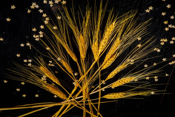 Yatay bileşim hala siyah yanmış tahtaların ve pasta yıldızlarının arka planında buğday kulaklarıyla yaşam