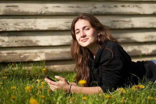 Young Brunette Girl Black Jacket Lying Green Grass Holding Phone — Stock Photo, Image