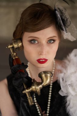 Kırmızı dudaklı, siyah retro elbiseli, şapkalı güzel esmer kadın. Eski bir telefonu tutup doğrudan kameraya bakmak, konuşmak.                        