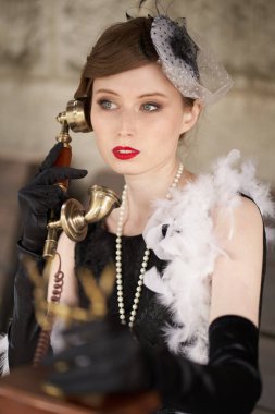 Kırmızı dudaklı, siyah retro elbiseli, şapkalı güzel esmer kadın. Eski bir telefonu tutup başka bir yere bakıyorsun.                               