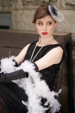 Kırmızı dudaklı, siyah retro elbiseli, şapkalı güzel esmer kadın. Bir bankta oturup başka tarafa bakıyor.                               