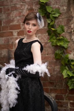 Siyah retro şapkalı güzel bir esmer dikilip doğrudan kameraya bakıyor. Duvara yaslan. Tarihi yeniden yapılandırma                               