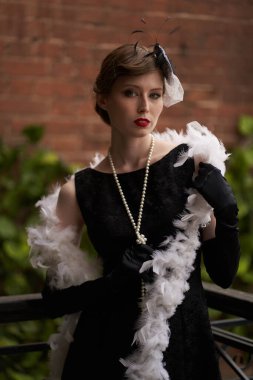 Siyah retro şapkalı güzel bir esmer dikilip doğrudan kameraya bakıyor. Duvara yaslan. Tarihi yeniden yapılandırma                               