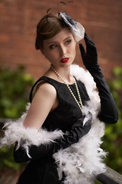 Siyah retro şapkalı güzel bir esmer duruyor ve başka tarafa bakıyor. Duvara yaslan. Tarihi yeniden yapılandırma                               