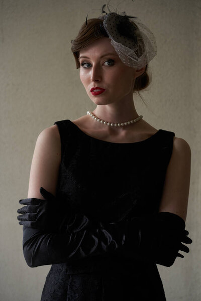 Portrait of a Beautiful brunette in a black retro hat stands and looks directly at the camera. Against a white wall. Historical reconstruction                               