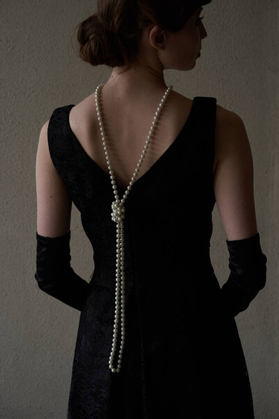   A beautiful brunette in a black retro hat is standing with her back to the camera, looking away. Historical reconstruction                             