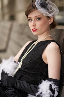  Kırmızı dudaklı, siyah retro elbiseli, şapkalı güzel esmer kadın. Oturup başka tarafa bakıyor.                              