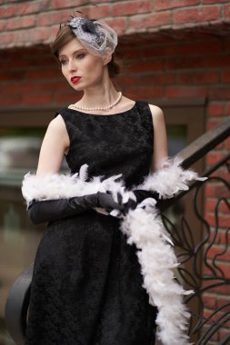 Siyah retro şapkalı güzel bir esmer duruyor ve başka tarafa bakıyor. Duvara yaslan. Tarihi yeniden yapılandırma                               