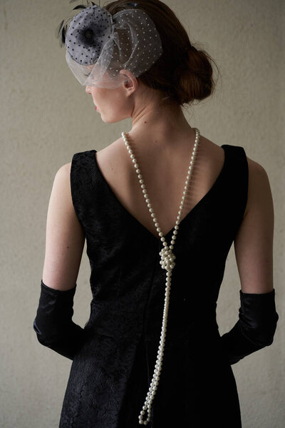 A beautiful brunette in a black retro hat stands with her back to the camera. Historical reconstruction                               