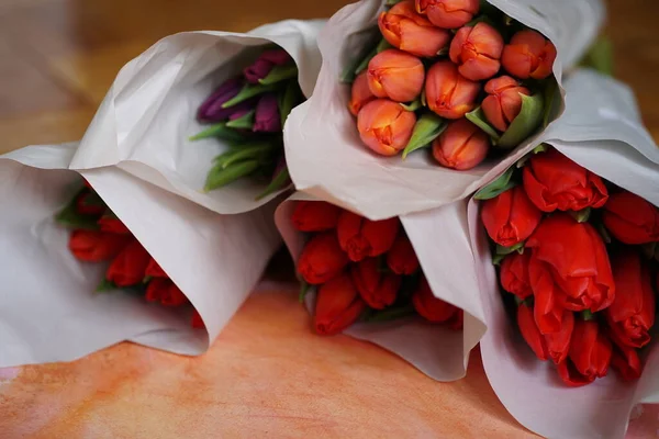 Colorful bouquets of tulips in paper packaging, lying on a wooden table