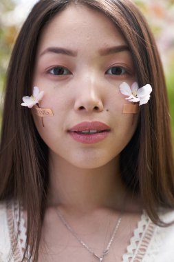  Beyaz elbiseli güzel bir Asyalı kadının portresi, beyaz çiçeklerle bir ağacın yanında duruyor, doğrudan kameraya bakıyor.                              