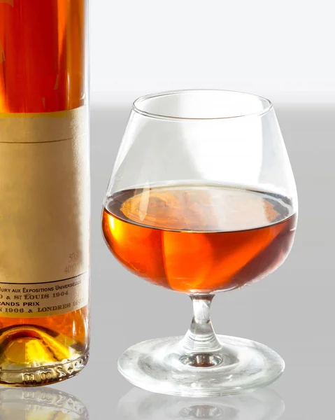 Glass with cognac and bottle on white and gray