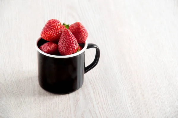 Frische reife Erdbeeren im schwarzen Metallbecher auf hölzernem Hintergrund — Stockfoto