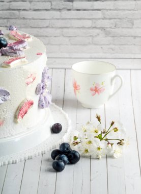 Beyaz süslemeli ev yapımı kek, mavimsi, kiraz çiçeği ve bardak.