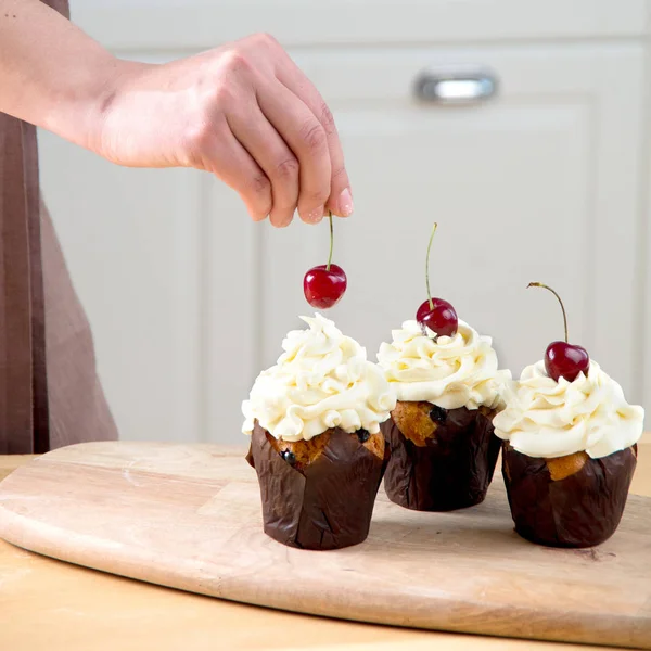 Kvinnlig bagare dekorerar cupcake med körsbär och crème — Stockfoto