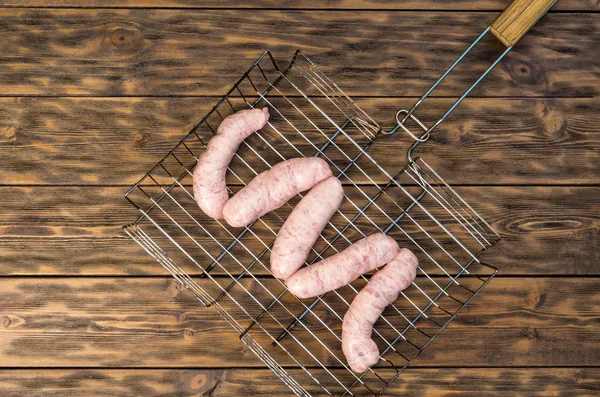 Sausages on grate for frying on wooden background — Stock Photo, Image
