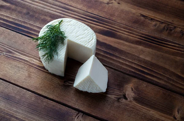 Koyu ahşap tahta üzerinde ev yapımı peynir tekerleği ve yeşillikler