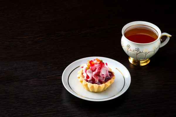 Basket-cake with jam on the plate and tea cup on dark background