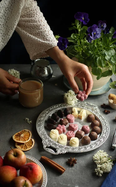 On the table is a plate with chocolates, cocoa, flowers and nuts. Hand takes candy.