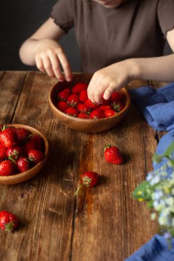 Bir çocuk ahşap bir masada oturur ve çilek yer..