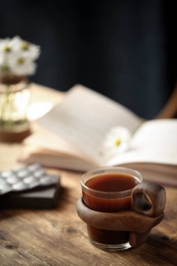Masanın üzerinde çikolata, kitap ve çiçeklerle birlikte güzel bir fincan kahve var..