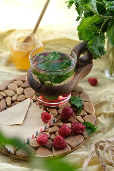 Fruit tea with raspberries and mint berries in a glass cup, honey and lemon.