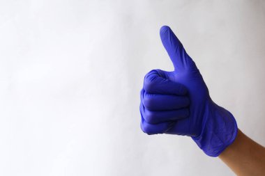 Eller mavi cerrahi eldivenlerde. Yeşil tıp eldivenlerinden yapılmış işaret simgesi gibi. Baş parmak işareti. İyi niyet göstergesi. Beyazda izole edilmiş