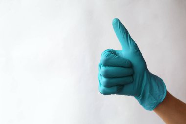 Eller turkuvaz cerrahi eldivenlerde. Yeşil tıp eldivenlerinden yapılmış işaret simgesi gibi. Baş parmak işareti. İyi niyet göstergesi. Beyazda izole edilmiş
