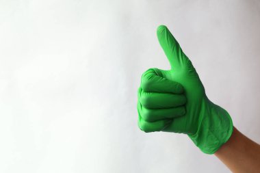 Elleri yeşil cerrahi eldivenlerde. Yeşil tıp eldivenlerinden yapılmış işaret simgesi gibi. Baş parmak işareti. İyi niyet göstergesi. Beyazda izole edilmiş