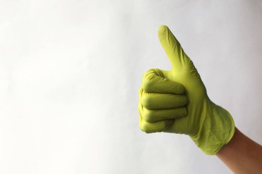 Elleri sarı cerrahi eldivenlerde. Yeşil tıp eldivenlerinden yapılmış işaret simgesi gibi. Baş parmak işareti. İyi niyet göstergesi. Beyazda izole edilmiş