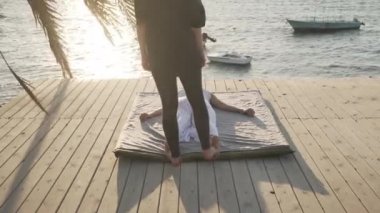 Genç bir kadın güneş doğarken ahşap zeminde masaj yapıyor.