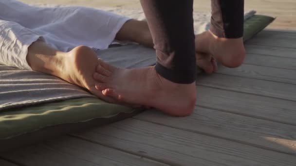 Молода жінка робить масаж для ніг на дерев'яній підлозі на сході сонця — стокове відео