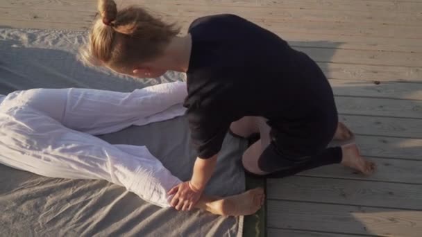 Молода жінка робить тайський масаж йоги на дерев'яній підлозі на сході сонця — стокове відео