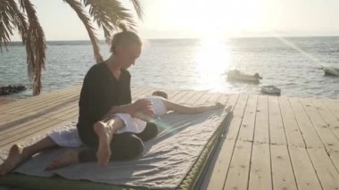 Genç bir kadın güneş doğarken ahşap bir zeminde Tayland yogası yapıyor.